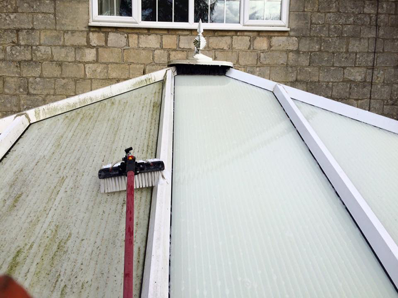 Conservatory roof mid-clean — left side green with algae, right side restored to clear panels